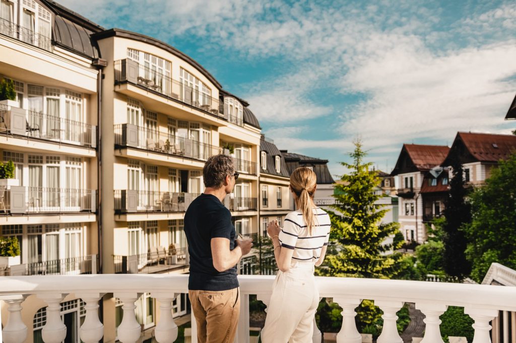 Pár na balkoně hotelu s výhledem na lázeňské domy