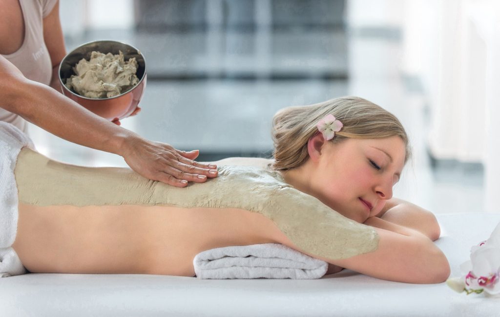 Žena relaxuje při jílovém zábalu zad ve wellness Rogaška Slatina, terapeutka nanáší léčivý jíl