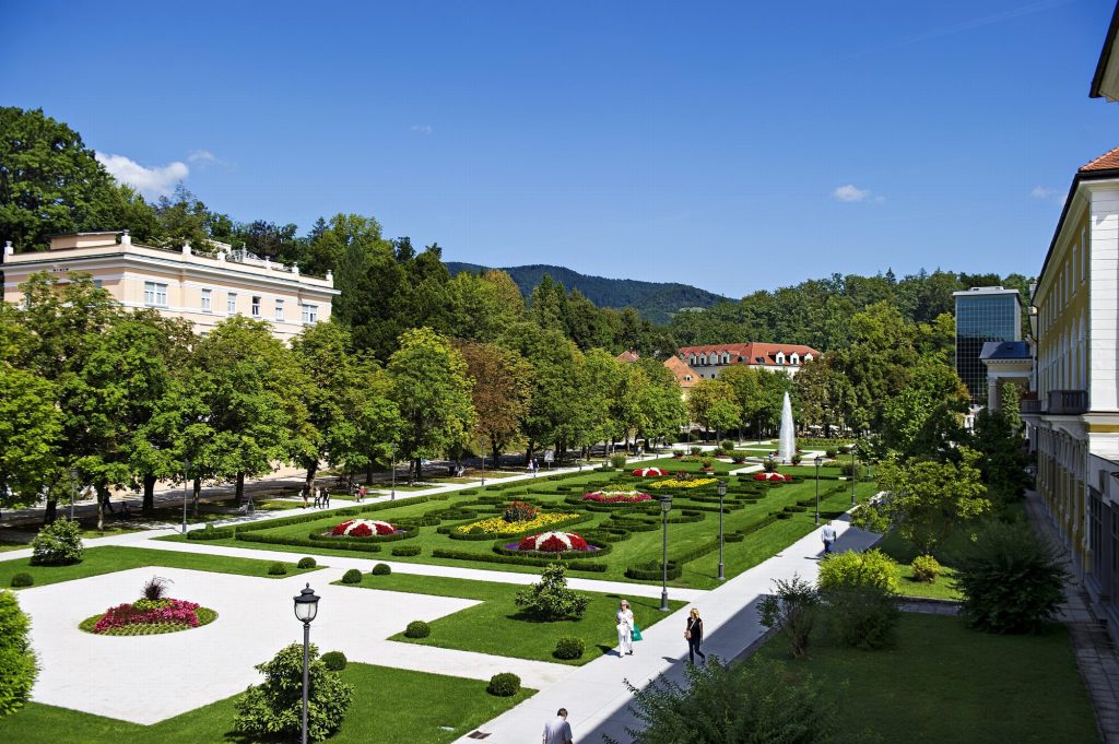 Lázeňský park Rogaška Slatina s ornamentálními záhony, fontánou a procházejícími hosty
