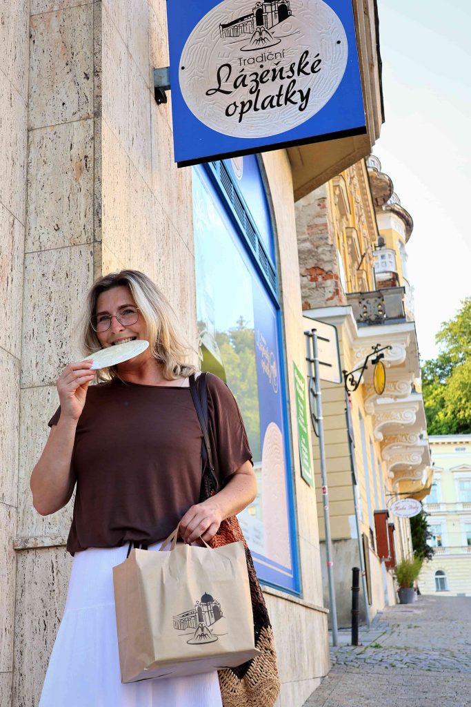 Žena ochutnává tradiční lázeňskou oplatku před kolonádou v Mariánských Lázních