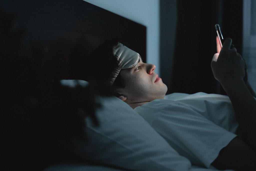 Muž v posteli v noci sleduje telefon, nemůže usnout